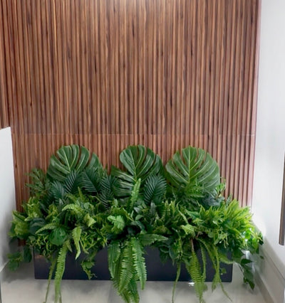 Artificial green plants in a black planter against a wooden panel background